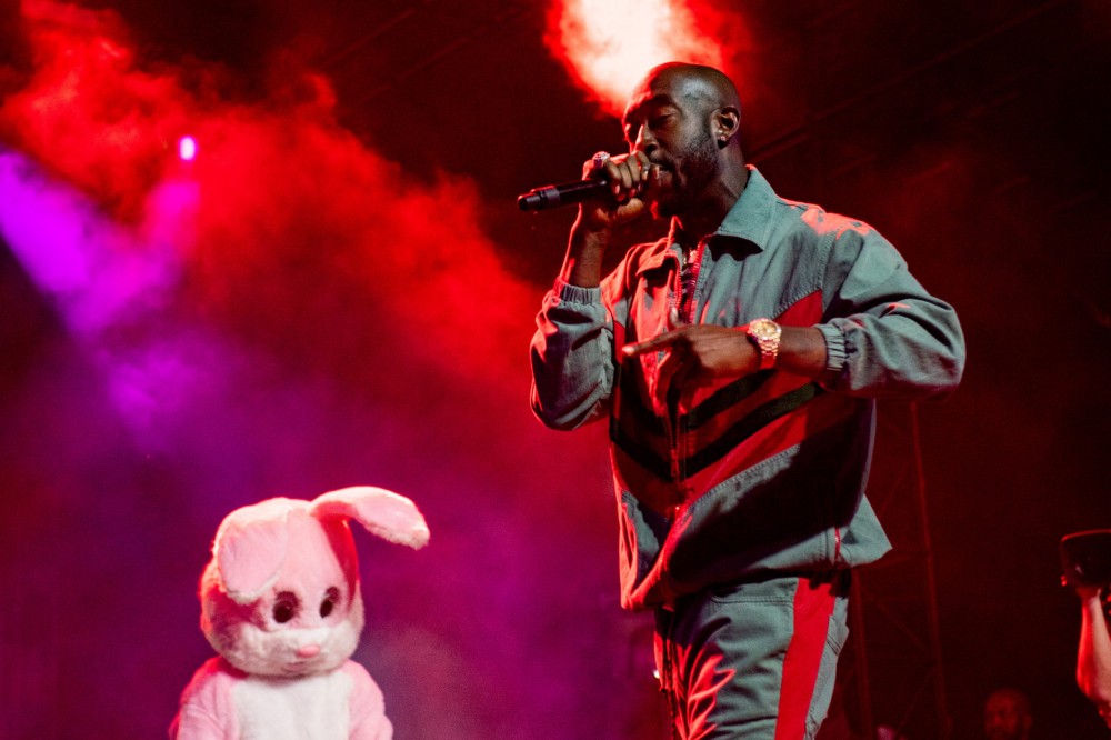 Freddie Gibbs wearing a tan two piece while performing on stage in front of a pink bunny.