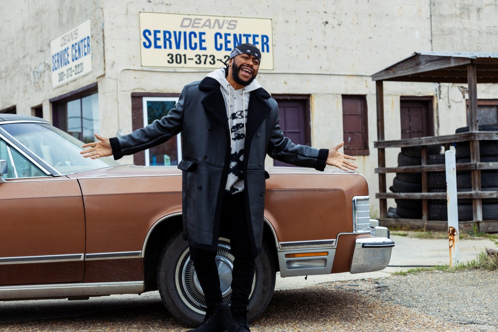 Raheem DeVaughn singing in front of brown car